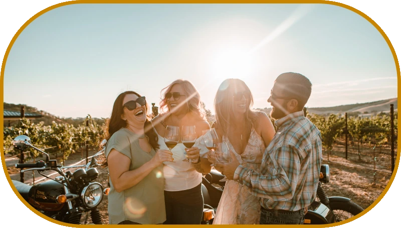 Four friends laughing together with glasses of wine beside the sidecar at golden hour