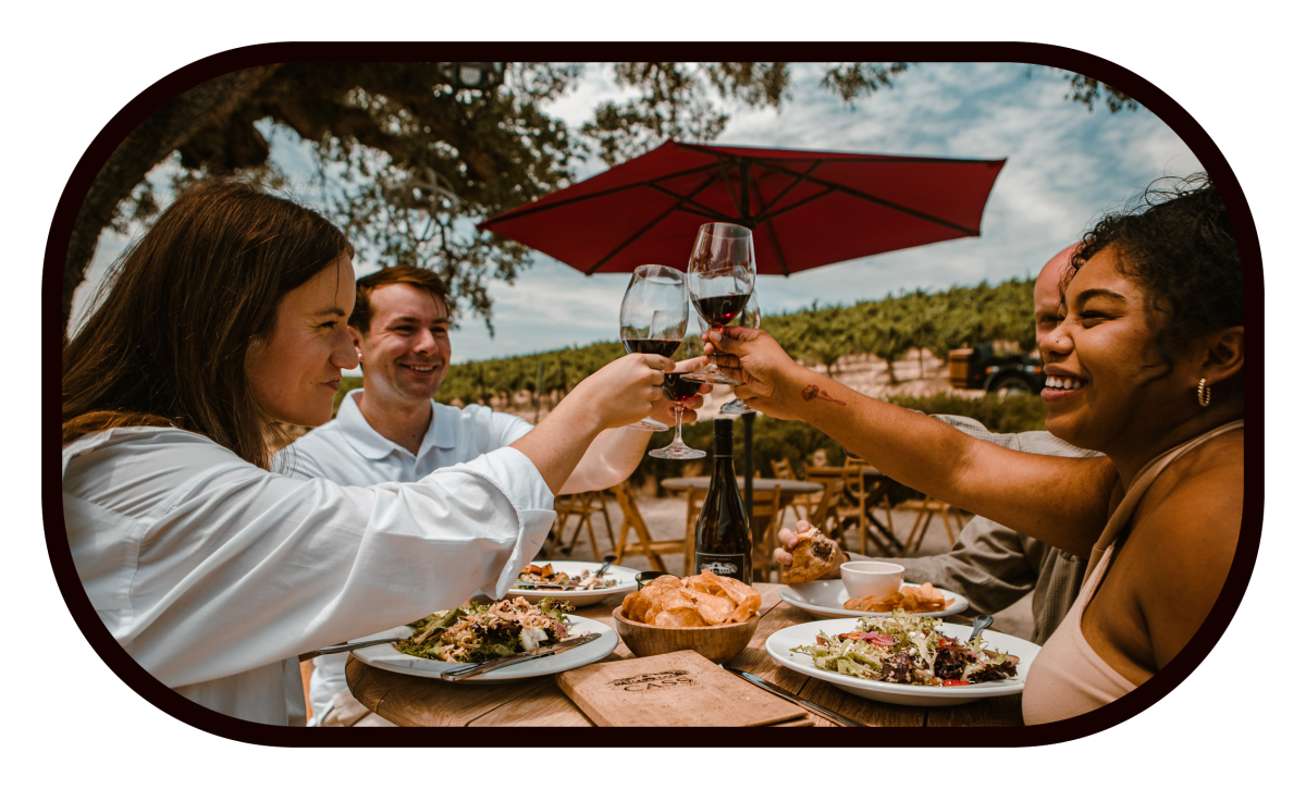 Friends toasting over a table of food under a red umbrella at the winery
